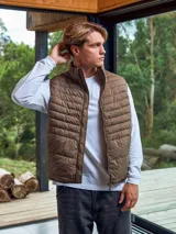 Chaleco acolchado marrón sin mangas con cuello alto y cierre lateral oculto y cremallera frontal. Bolsillos frontales y diseño plegable para fácil almacenamiento.