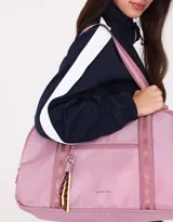 Bolso color beige de tela deportiva con manijas superiores y cierre superior. Tiene un bolsillo frontal con cierre y bolsillos laterales con cierre y tiradores de cordón y goma.