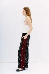 Pantalón de viscosa con estampado abstracto en tonos mostaza, negro y rojo. Tiene tiro medio, calce amplio, cintura elastizada y bordados de lentejuelas.