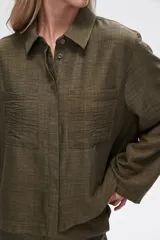 Camisa color natural de poliéster con cuello camisero, cierre con botones, dos bolsillos frontales y corte ancho.