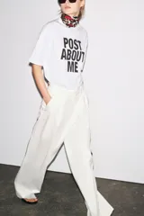 Camiseta blanca de corte amplio, cuello redondo y mangas cortas. Estampado frontal con la frase "Post About Me" en letras negras.