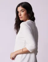Blusa blanca de poliéster y elastano, con cuello a la base, escote en V y mangas tres cuartos. Presenta dos bolsillos frontales con cierre metálico dorado.