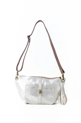 Bandolera tipo sobre o clutch, color beige metalizado o champagne, con textura brillante/iridiscente. Posee un bolsillo frontal con cierre de broche giratorio y un detalle de borla colgante en uno de los laterales. La correa es de cuero marrón oscuro.