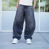 Pantalón de jean negro con lavado oscuro y efecto desgastado, de corte ultra ancho y tiro alto. Presenta un parche circular con logo en el bolsillo trasero derecho.