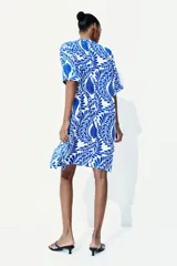 Vestido túnica a la rodilla en tejido liviano de viscosa con cuello mao y abertura en V. Modelo de corte holgado con hombros levemente caídos, mangas cortas y bajo recto con tajos laterales. Estampado con motivos florales en azul y blanco.