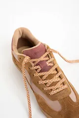 Zapatilla deportiva de caña baja, con paneles combinados en gamuza color camel y material liso color rosado pálido. El cuello y el talón son de color vino o rosado oscuro. Cordones trenzados en tonos beige y naranja. Suela de goma color camel.