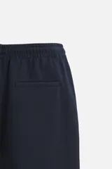 Pantalón negro de corte cropped, con cintura elástica ajustable con cordón, bolsillos laterales y traseros de vivo. El bajo tiene terminación con vuelta.