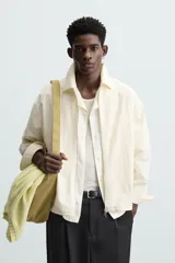 Sobrecamisa color crema de tejido técnico ligero, corte regular fit, cuello solapa, manga larga con puño abotonado, bajo ajustable con elástico en laterales y cierre frontal con cremallera.