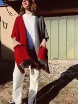 Ruana tejida a crochet, mitad roja y mitad gris, con bolsillos y flecos.