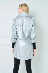 Campera plateada de poliéster con capucha ajustable y cintura con cordón ajustable interno. Cuenta con cierre frontal con botones a presión, bolsillos laterales con cierre y mangas 3/4 con puños elásticos.