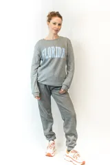 Sweater gris de corte clásico con cuello redondo y puños y cintura acanalados. Estampado frontal con la palabra "Florida" en letras celestes con borde blanco.