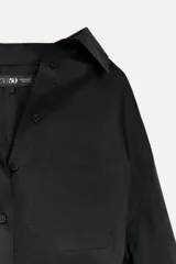 Camisa negra de algodón con cuello solapa, manga larga tipo murciélago con puños abotonados, hombros caídos, bolsillo de parche en el pecho, pinzas en la espalda y cierre frontal con botones.