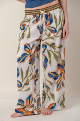 Pantalón de tejido ligero color blanco con estampado de flores en tonos azul, naranja y verde. Tiene cintura elastizada con cordón ajustable.