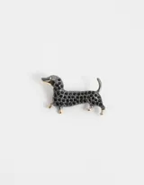Pin prendedor con forma de perro salchicha, con cuerpo cubierto de strass negros y detalles dorados en hocico y patas.