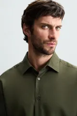 Camisa negra de manga larga con cuello italiano y cierre frontal de botonadura. Presenta un tejido con estructura de fácil cuidado.