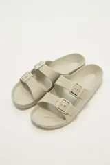 Sandalias bajas color beige con dos tiras anchas con hebillas ajustables.