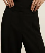 Pantalón wide leg negro de crepé, con cintura alta, pliegues, botón y trabillas.