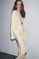 Sweater color crema de tejido de punto liso, con cuello barco y mangas anchas que se estrechan hacia la muñeca.