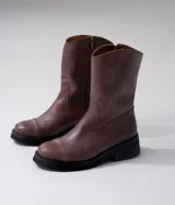 Bota de cuero vacuno color marrón, con caña media, suela de caucho y punta redonda.