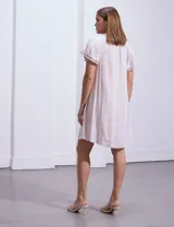 Vestido corto de lino a rayas verticales color lila y blanco, con cuello fruncido, escote en V y lazo de ajuste. Mangas cortas con puntilla de crochet.