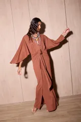 Vestido largo tipo kimono de color marrón, confeccionado en tela de punto texturada. Posee mangas amplias y abiertas, escote en V pronunciado y un lazo ajustable en la cintura para definir la silueta.