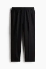 Pantalón de vestir negro, tobillero, de corte slim fit, con elástico y cordón ajustable en la cintura, bolsillos laterales y traseros ribeteados, pliegues y doblez en el bajo.