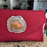 Sobre de fiesta rojo oscuro, tejido artesanalmente en la India, con cierre de solapa y broche magnético. Presenta un ágata central con borde dorado. Incluye asa de cadena dorada para llevar al hombro.