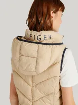Chaleco acolchado Tommy Hilfiger color beige con capucha ajustable con cordones y cierre de cremallera frontal. Cuenta con bolsillos laterales con cremallera y detalles distintivos de la marca.