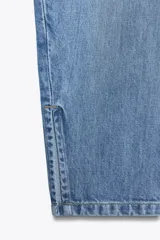 Pantalón de jean celeste de tiro medio, corte amplio tipo globo, con bolsillos delanteros y traseros, trabillas en la cintura, abertura lateral en el ruedo y cierre frontal con cremallera y botón.