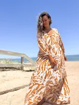 Vestido largo de corte amplio con estampado floral en tonos beige y blanco. Tiene escote en V con lazos y mangas largas abullonadas.