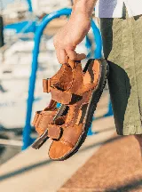 Sandalias de cuero color marrón con tiras ajustables con velcro y suela de goma negra.