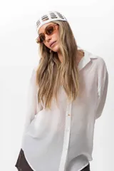 Camisa blanca traslúcida de seda ligera, de textura suave y caída fluida, con cuello clásico y cierre frontal con botones dorados.