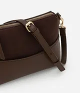 Cartera transversal pequeña color marrón, con la parte superior de gamuza y la inferior de cuero sintético. Tiene cierre de cremallera metálica dorada y asa larga ajustable y desmontable con mosquetones dorados.