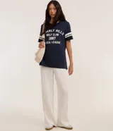Remera azul marino de algodón con cuello en V y mangas cortas con rayas blancas. Estampa frontal con texto "Beverly Hills Golf Club 1997 Local League" en blanco.