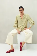 Camisa celeste de manga larga con cuello redondo y escote en V. Presenta detalles de pasamanería en el frente y las mangas, y botones forrados al tono. De corte fluido.