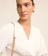 Blusa blanca de crepé con escote en V sobrepuesto, mangas cortas y recorte en la cintura con aspecto de volado.