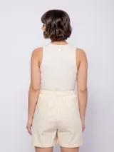 Bermuda color crema de algodón, con bolsillos laterales y traseros, y cierre frontal con tres botones veteados. Cuenta con elástico en la pretina trasera.