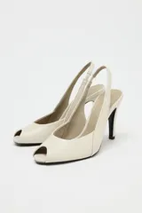 Zapato de tacón en piel color beige con abertura lateral, punta fina y cierre con tira ajustable. Tacón alto fino de 10,5 cm.