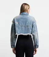 Campera cropped de jean celeste con cuello solapa, cierre frontal con botones, mangas largas, barra deshilachada con flecos y detalles de roturas.