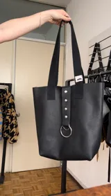 Bolso tote negro de cuero con asas cortas y largas. Presenta un bolsillo interno y cierre con dos botones.