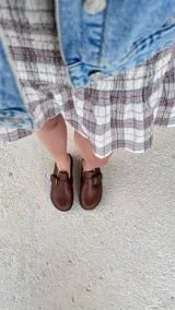 Zuecos color marrón con punta cerrada redondeada y tira con hebilla ajustable sobre el empeine. Poseen suela de goma negra y plantilla anatómica.