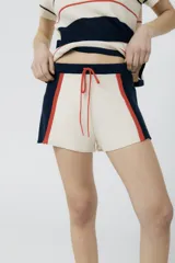 Short tejido en jersey color crudo con cintura y laterales en azul marino y rayas verticales rojas.