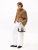 Cartera de lona color beige con rayas verticales azul marino y plateada. Tiene asa superior y correa extraíble y ajustable. El cierre es con solapa magnética y tiene el logo de Tommy Hilfiger en dorado.