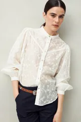 Camisa blanca con bordado floral en contraste, cuello mao, abotonadura frontal y mangas largas con frunces en los hombros.