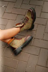 Botas de caña media con plataforma, confeccionadas en tweed a cuadros rojos y negros, con detalles en cuero marrón y cordones marrones.