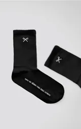 Medias negras de algodón, estilo 3/4, con puño acanalado. Presentan un bordado blanco en la parte superior que simula unas tijeras cruzadas y texto en la planta que dice "Ropa sin género para seres humanos".