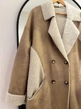 Tapado largo color beige, con interior y exterior de gamuza sintética y detalles de corderito sintético en cuello, bolsillos y puños. Cierre frontal con doble botonadura.