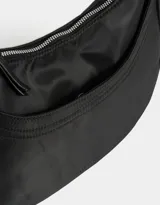 Bandolera hobo negra de tela deportiva con correa regulable, cierre superior, bolsillo frontal y charm lateral decorativo.