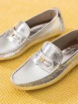 Mocasín de cuero vacuno color marrón con textura croco y acabado brillante. Incluye aplique metálico en forma de corazón sobre el frente y suela de goma.