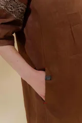 Vestido largo color beige, confeccionado en lino, con escote en V con volados y apliques de puntilla en las mangas. Posee bolsillos delanteros y tajos laterales.